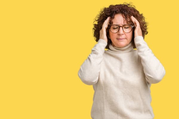 Woman with curly hair and glasses with both hands on head, headache, migraines, migraine research